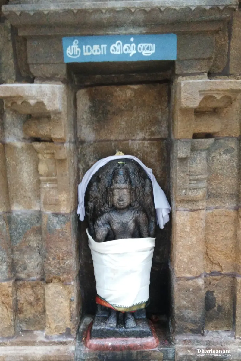 A small stone Mahavishnu in a wall niche, draped in white cloth, with a name board above