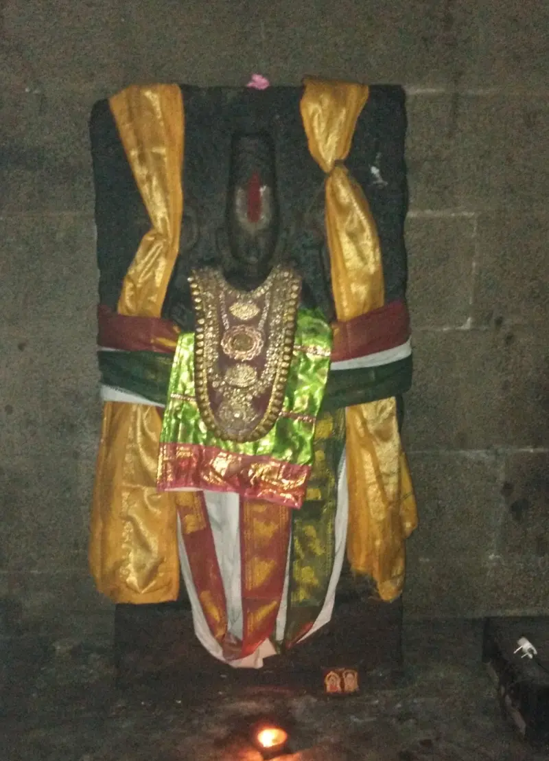 A dark stone idol wrapped in yellow, green and red silks with a gold necklace, a lamp lit below