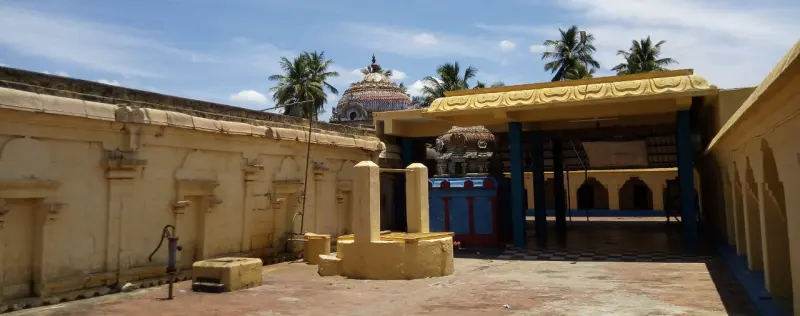 Open courtyard with a small stone structure at the centre and a blue-pillared hall at the right