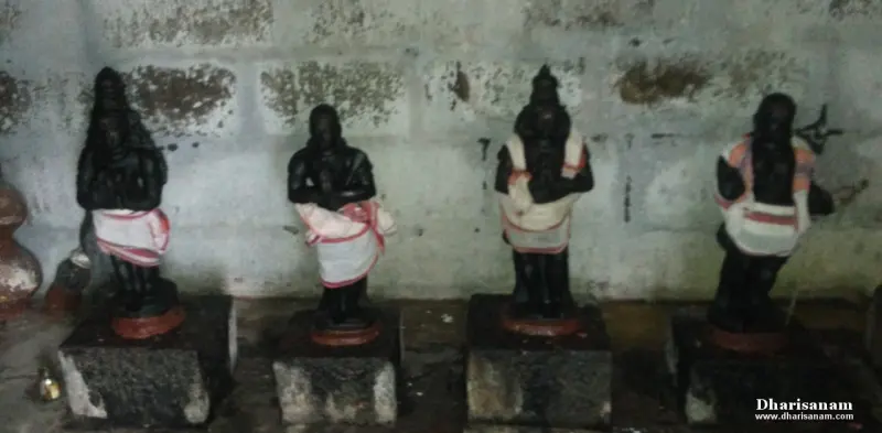 Four small black idols in red and white cloth stand in a row on stone bases.