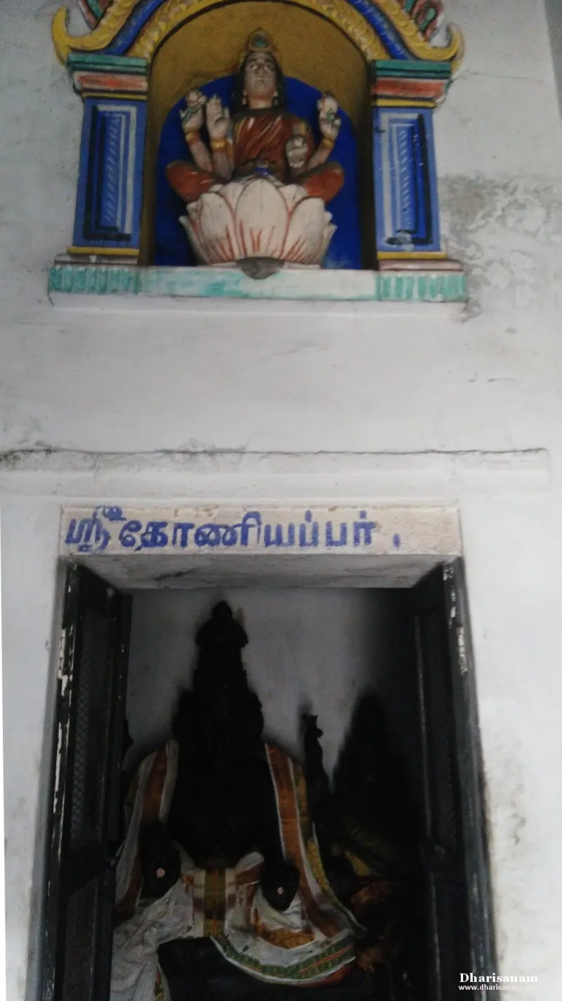 A painted figure seated on a lotus above a doorway with a Tamil name board and a dark idol inside