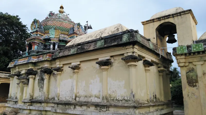 The side of a yellow sanctum wall with pillars under a coloured tower, and a small bell tower to the right.