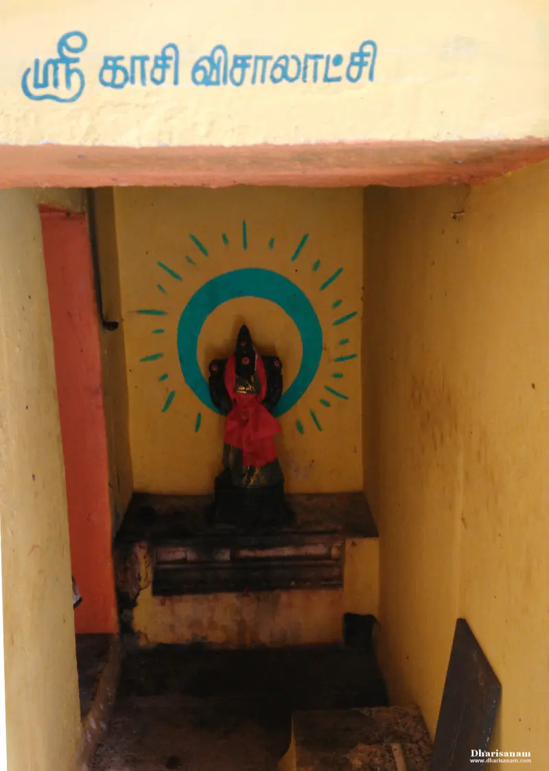 A small dark stone figure in red cloth in a yellow shrine with a green painted halo and a Tamil name board above