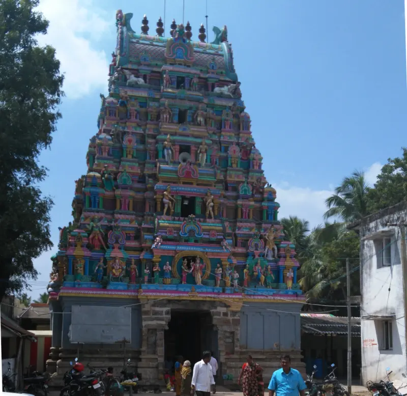 The tiered painted tower above a stone gateway; visitors walk past in the foreground and motorbikes are parked.