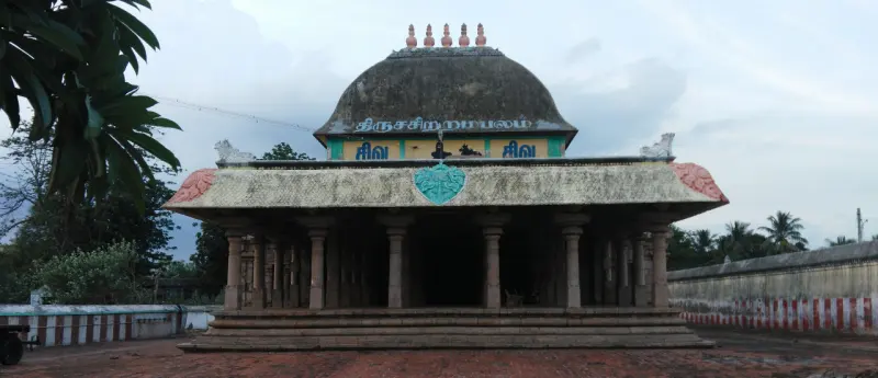 A hall with a dome-shaped roof and a curved front roof stands on a stone plinth in an open courtyard.