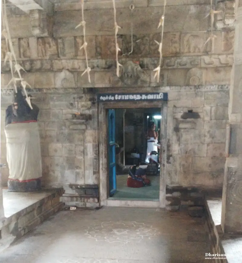A stone wall with a blue door open to the sanctum, a name board above it and a kolam on the floor