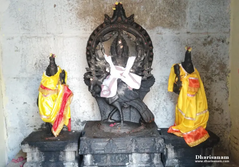 A dark stone figure on a peacock under a carved arch, with a smaller idol in yellow silk at each side