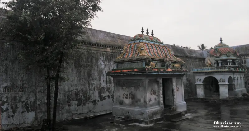 Two small shrines with painted roofs beside a tall weathered wall, a tree at left