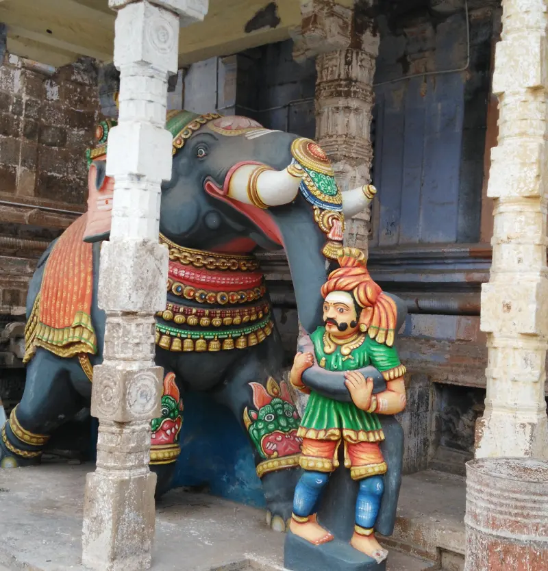 Colourful caparisoned elephant statue beside a mustached keeper
