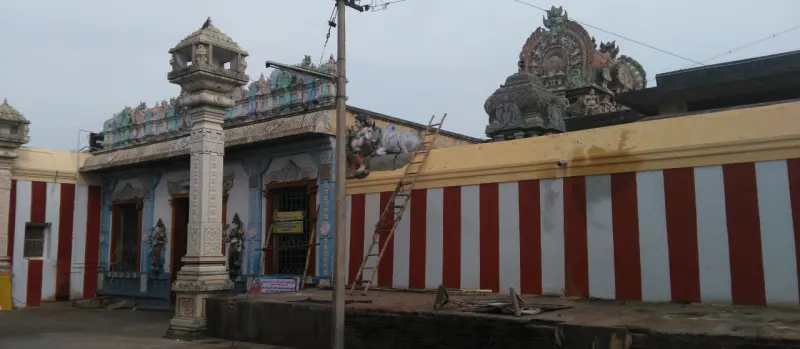 A blue shrine front beside a wall painted in red and white stripes, with a ladder against it.