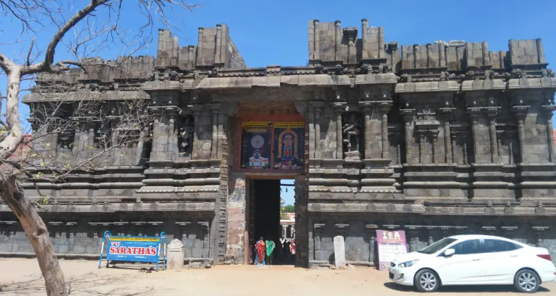 A massive stone gateway with a doorway at its base and a tree on the left; a white car is parked at right.