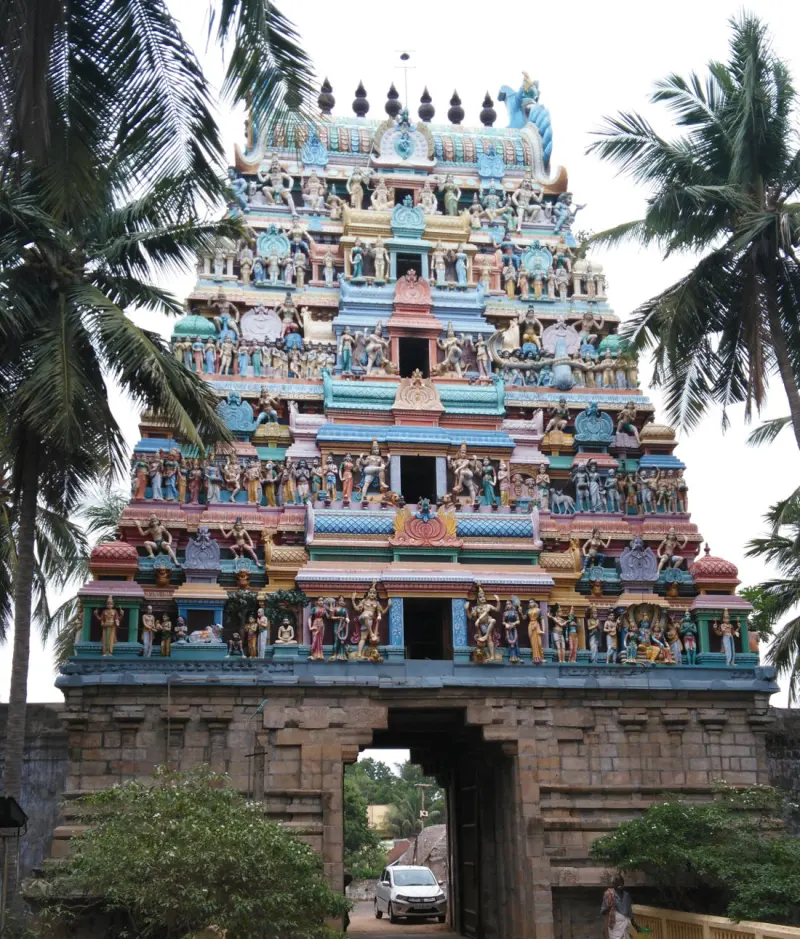 A tall tower covered in coloured figures rises above a stone gateway, with palm trees on both sides