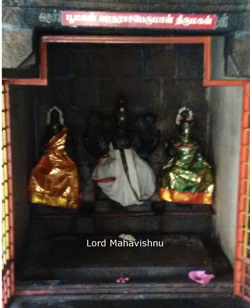 Three idols dressed in orange, white and green cloth, in a small shrine under a red name board