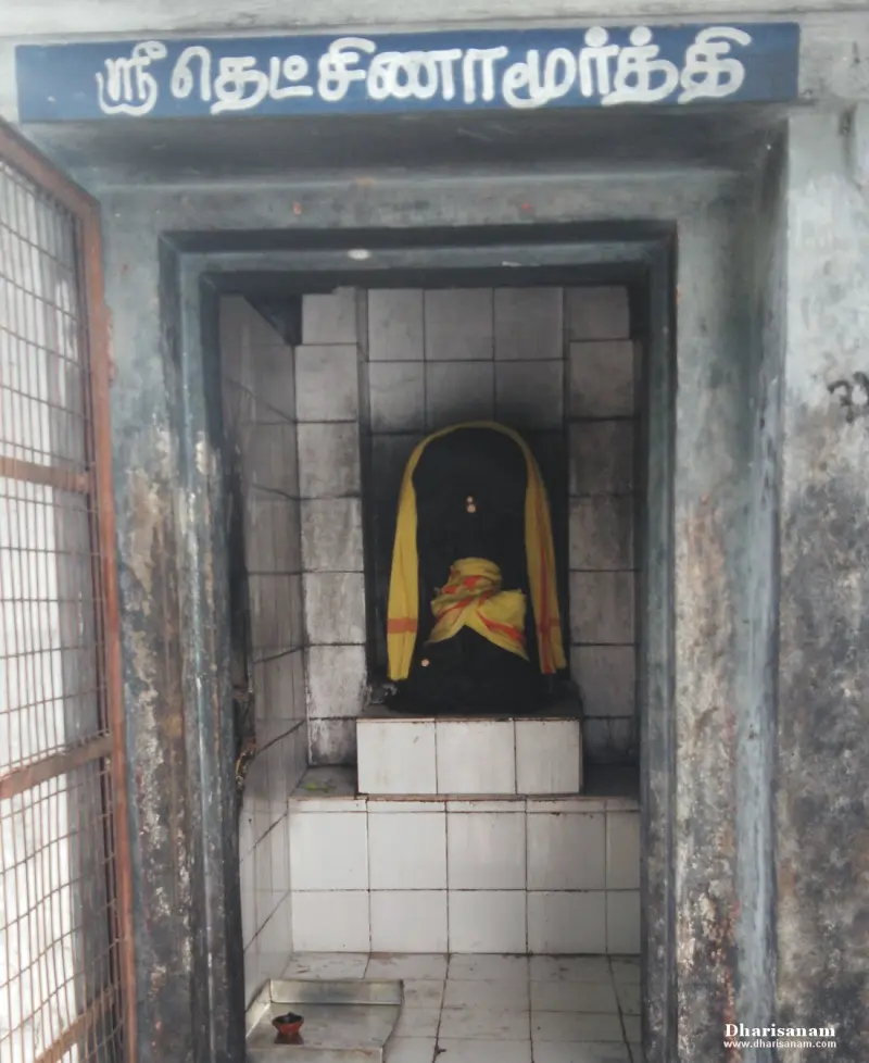 A tiled niche holding a dark stone figure with a yellow cloth, under a Tamil name board