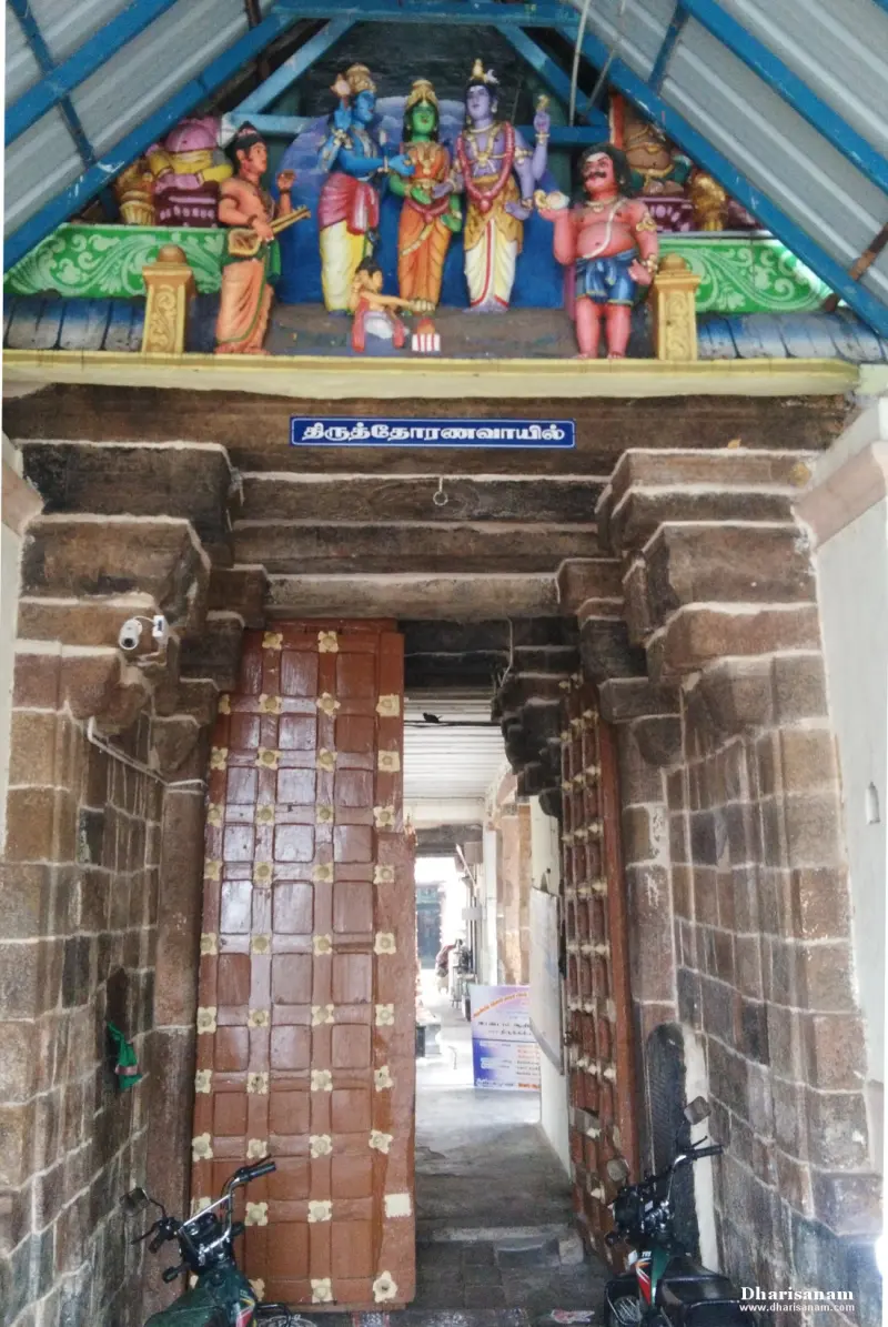 A stone gateway with brown wooden doors and a row of painted figures on the roof above it