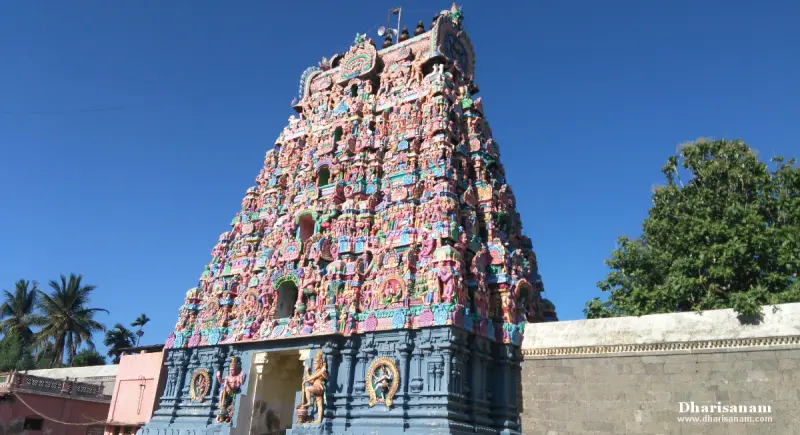 A tower of colourful sculptures against a blue sky, beside a grey stone wall.