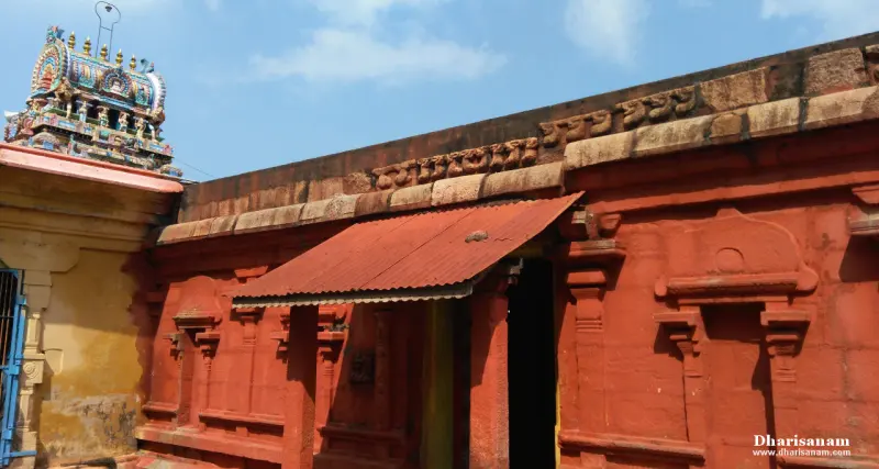 Red-painted wall with carved pilasters and a tin-roofed doorway; a tower top at the left