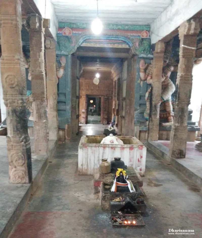 Stone pillars line a corridor with a Nandi and a lamp-lit altar in front of a distant doorway