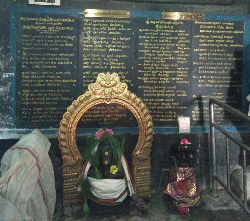 A small dark image under a gold arch, with Tamil hymn texts on black boards behind it.