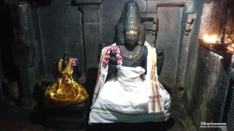 A dark stone idol in a white cloth and garland, seated beside a smaller idol wrapped in gold cloth.