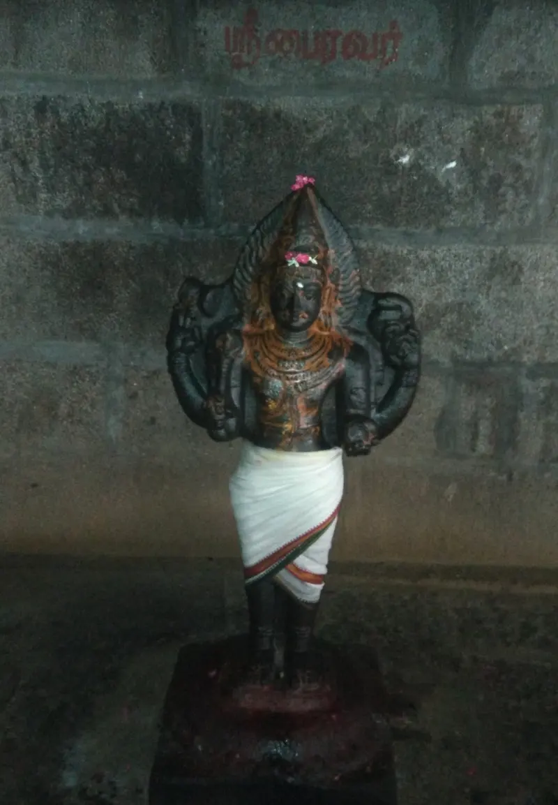 A black stone standing figure with several arms in a white cloth, name painted on the wall above