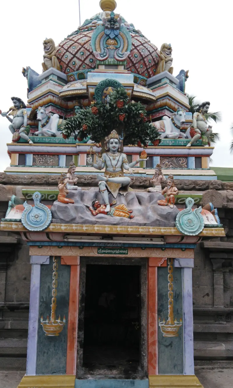 A shrine doorway with a painted tower above it showing a seated Dakshinamurthy under a tree, with sages around him.