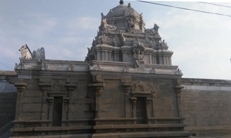 A stone shrine with a domed tower, a Nandi on its parapet and a long wall behind