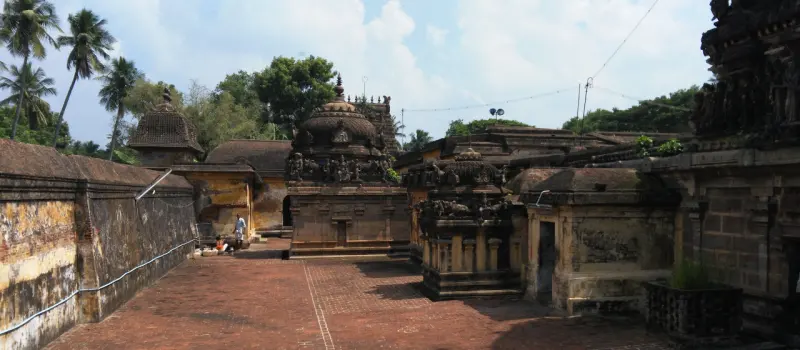 A wide brick-paved courtyard with several stone shrines and domed towers, trees and sky behind.
