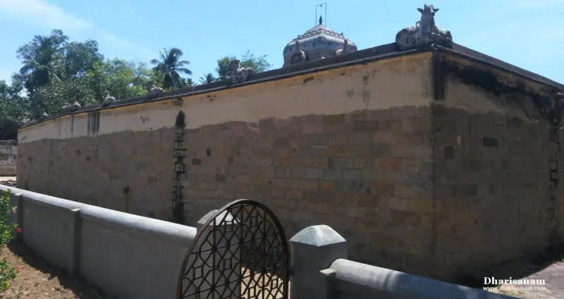 A long stone wall with Nandhi figures along its top edge, a small tower behind and a metal grille gate in front