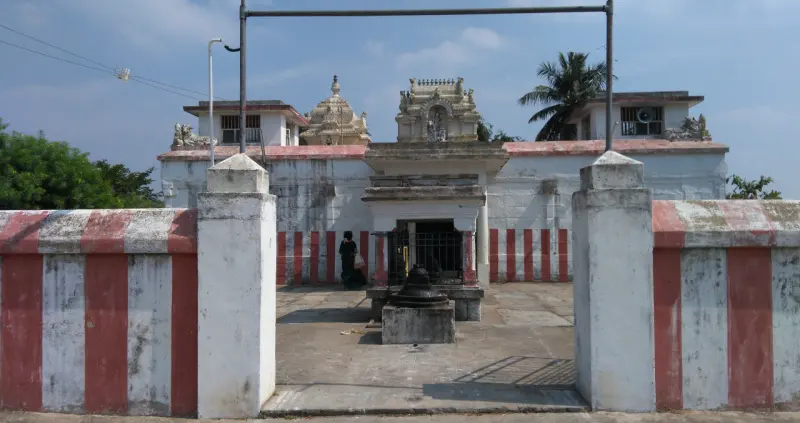 A courtyard seen between two striped gate pillars, with a small shrine and low towers behind
