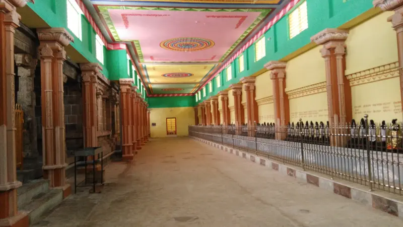 Wide corridor with orange pillars, a painted ceiling and a railing guarding a line of idols on the right.