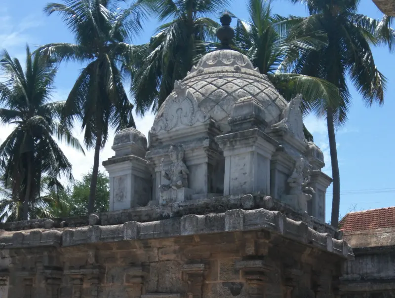 A stone shrine tower with a lattice-patterned dome and small corner towers, with tall coconut palms behind.