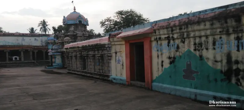 A long temple wall with an orange doorway and a painted Shivalingam, the sanctum tower rising behind.