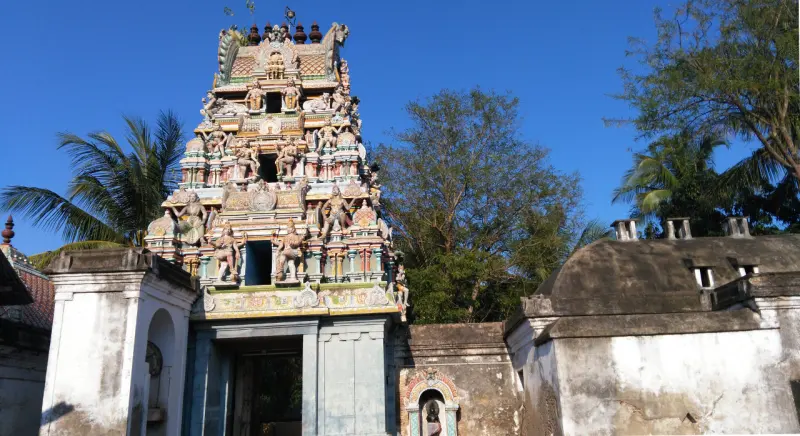 Colourful tiered gopuram with painted figures, trees and a domed building beside it