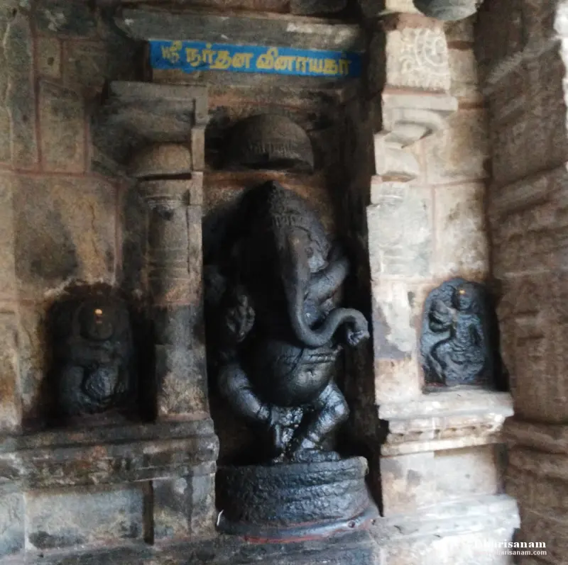 A black stone Vinayakar in a dancing pose, standing in a wall niche beneath a blue name board
