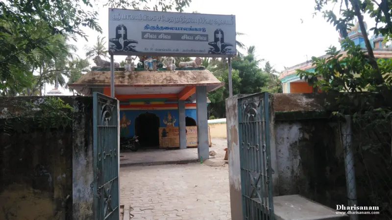 An open iron gate leads to a small entrance porch under a name board with two lingam drawings