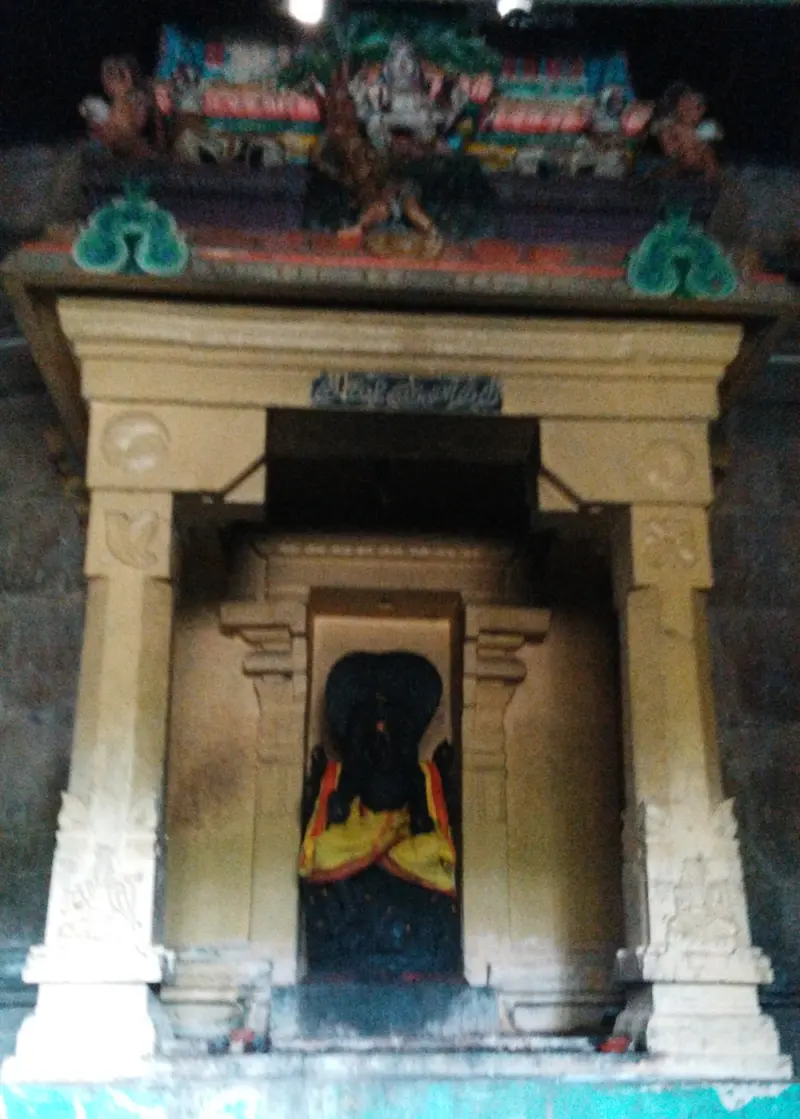 Dark shrine chamber with a black deity statue draped in yellow and red cloth