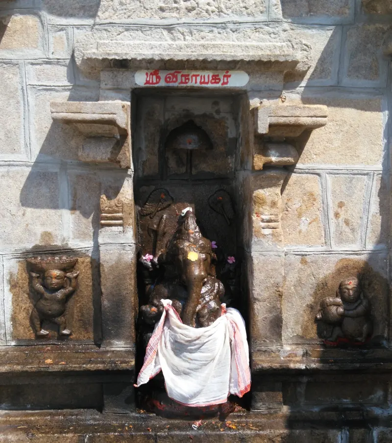 A stone Vinayakar draped in white cloth in a niche, with a small figure on each side