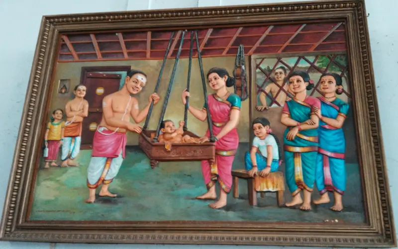 Framed painting of parents rocking a baby in a wooden cradle
