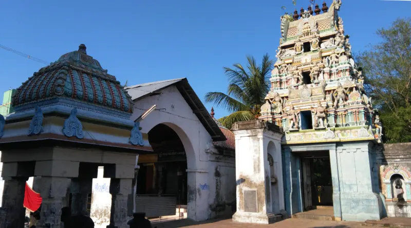 Tiered gopuram at right and a painted dome at left, under a clear blue sky