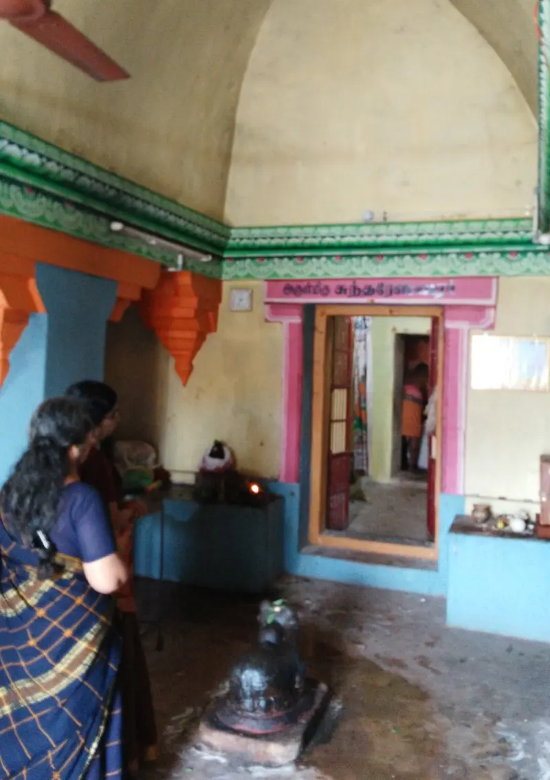 A Nandi faces the sanctum doorway inside a hall with a vaulted ceiling; two visitors stand beside it
