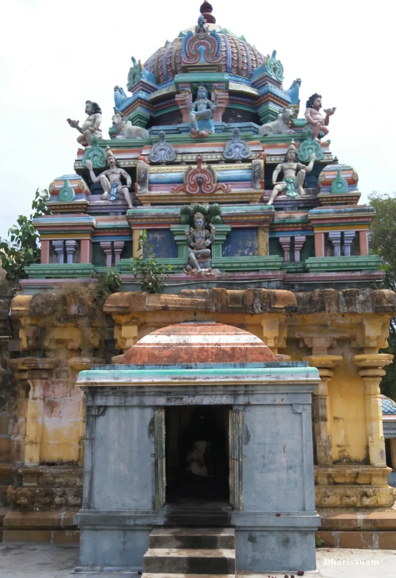 Colourful painted tower with figures behind a small grey shrine with a domed roof and an open door