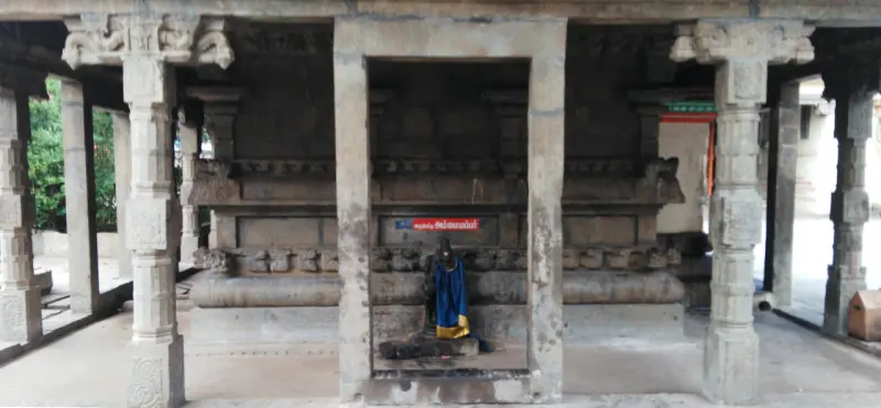 Pillared shrine entrance with a red name board and a small idol dressed in blue and yellow cloth