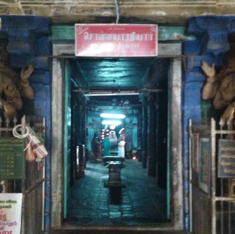 A dim doorway under a red Tamil name board leads down a pillared passage towards a lit inner shrine.
