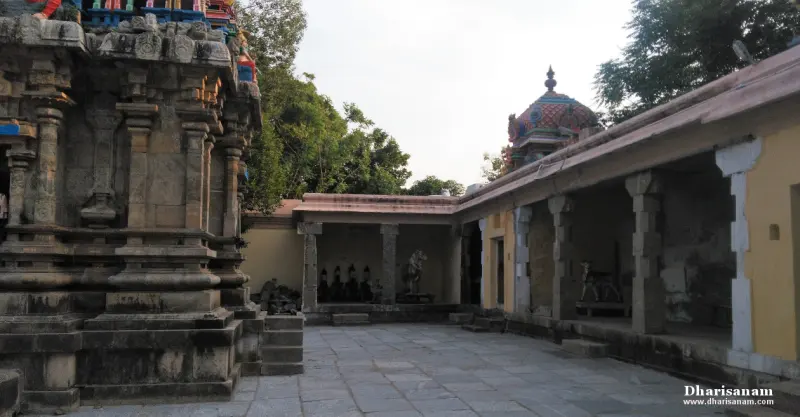 A paved courtyard with a stone building at left, a tiled-roof pillared corridor at right and a coloured dome behind