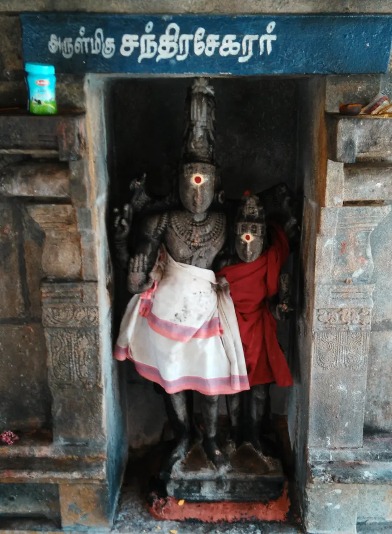 Stone Chandrasekarar with a smaller figure beside him in red cloth, in a niche beneath a blue name board