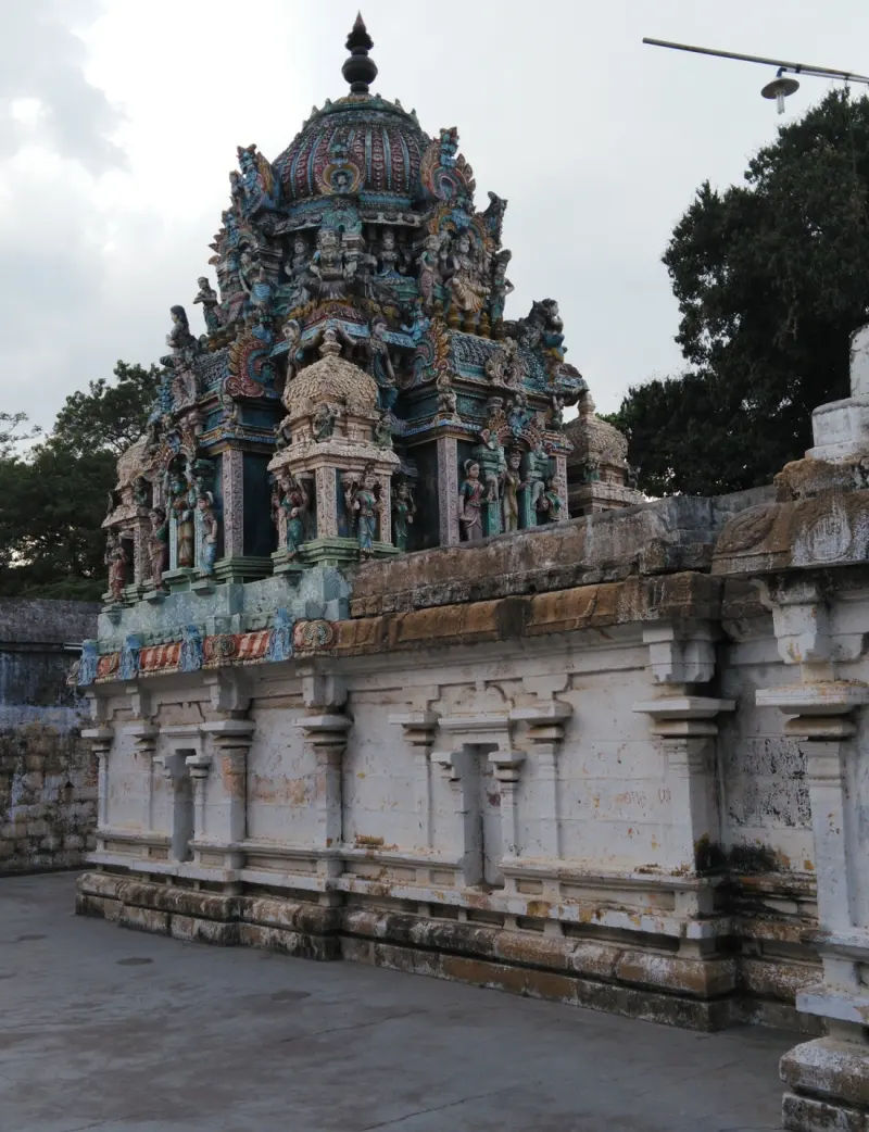 White stone wall with a tower of painted figures above, and a flat paved floor