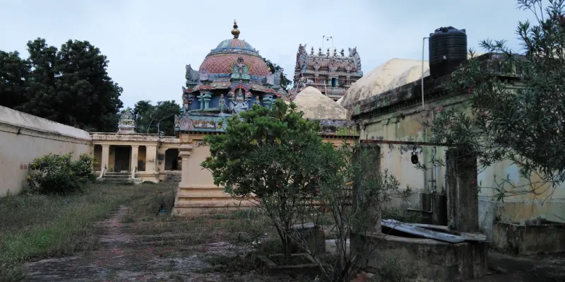 A grassy courtyard with shrubs, a domed sanctum tower, a gopuram behind and a water tank at right.