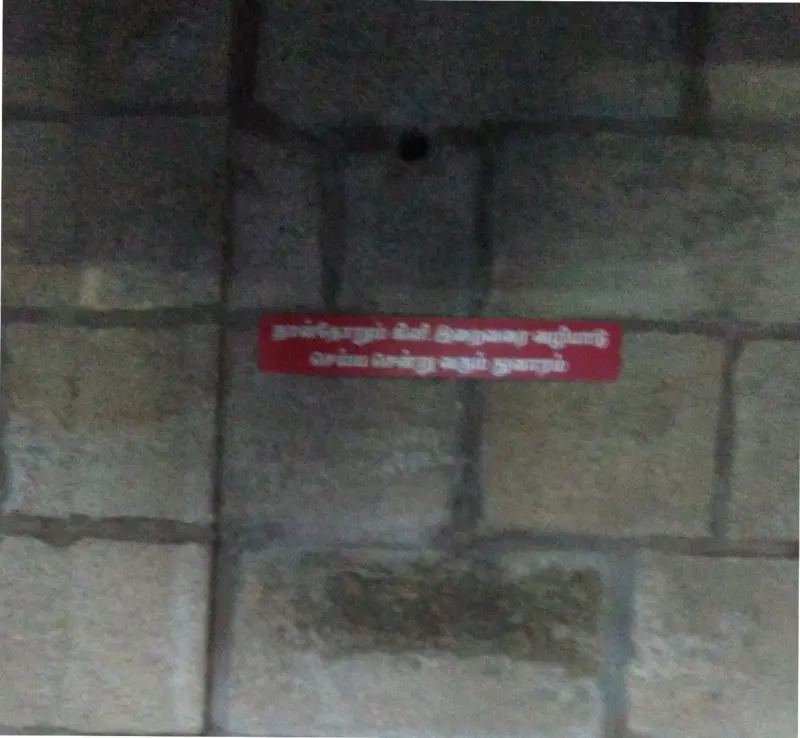 A dark round hole in a stone block wall, with a small red Tamil sign below it.