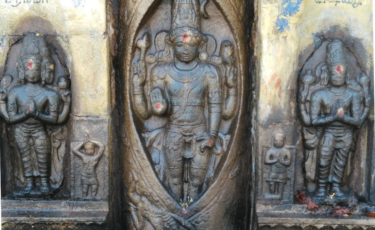 Stone relief of a standing four-armed figure in an oval niche, flanked by two smaller worshipping figures.